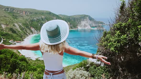 Excited Blonde Female Wearing Hat Spreading Arms on Viewpoint To Petani Beach on Kefalonia Island