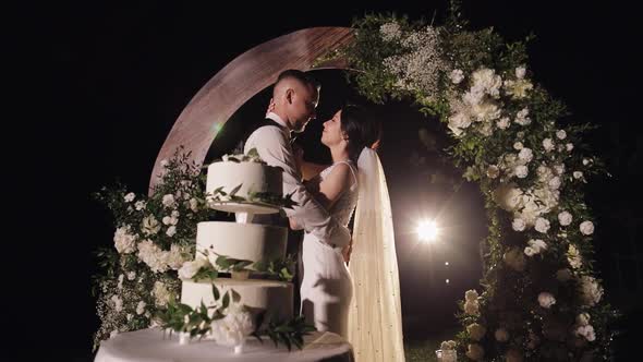 Newlyweds Making a Kiss Near Cake Lovely Bride and Groom Couple with Threetiered Wedding Dessert