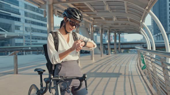 Asian businesswoman with backpack bicycle smil look smartwatch in city street go to work at office.