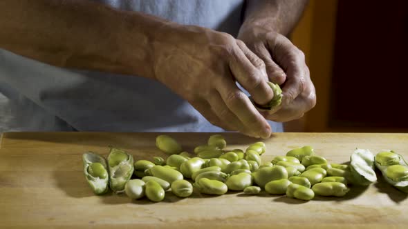 Wide, slider shot from left to right of a cutting board with shelled fava beans on the board and a m