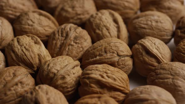Cinematic, rotating shot of walnuts in their shells on a white surface - WALNUTS