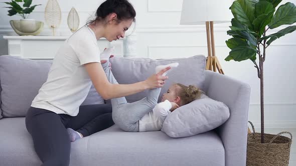 Young Mother Playing with Her Cute one year Daughter on the Couch at Home