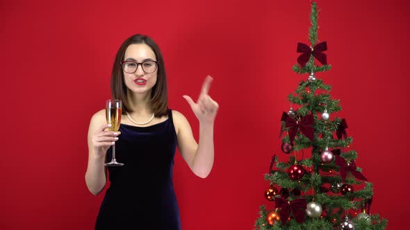 Young Woman Counts Five Seconds To the Holiday with a Glass of Champagne Near the Christmas Tree on