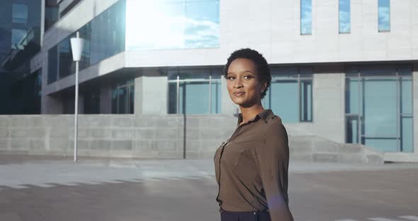 Smiling African Woman Walks on Street, Backdrop of City Building, Pulls Suitcase, Carries Tickets in