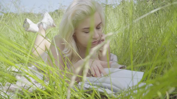 Absorbed Plus Size Woman Lying in Tall Green Grass and Reading Book. Portrait of Young Confident