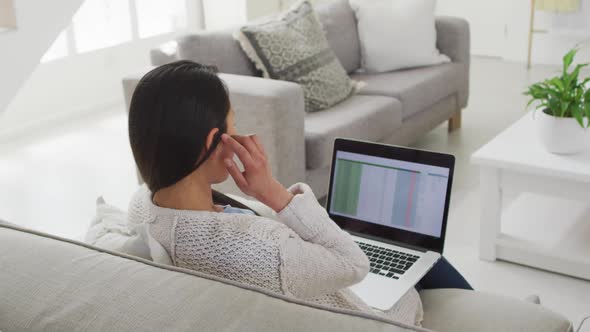Back view of asian woman sitting on sofa and working remotely from home with laptop