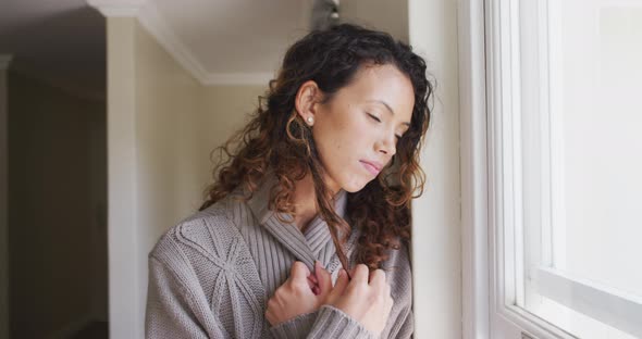 Thoughtful biracial woman standing at window and looking into distance