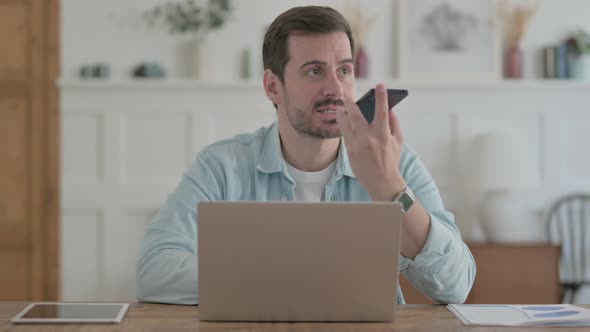 Upset Young Man Talking Angrily on Phone at Workplace