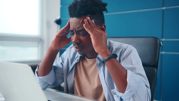 Young African American Man Experiencing Stress Sits at Desk in Home Office