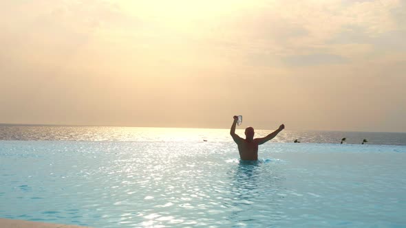 Man Having Fun in Outdoor Infinity Pool with Panoramic Sea View, at Sunrise, Travel and Vacation