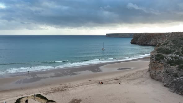 Aerial shot flying towards an anchored catamaran and surfers waiting for waves in a beautiful seclud