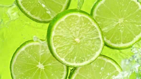 Super Slow Motion Shot of Lime Slices Falling Into Water on Green Background at 1000Fps