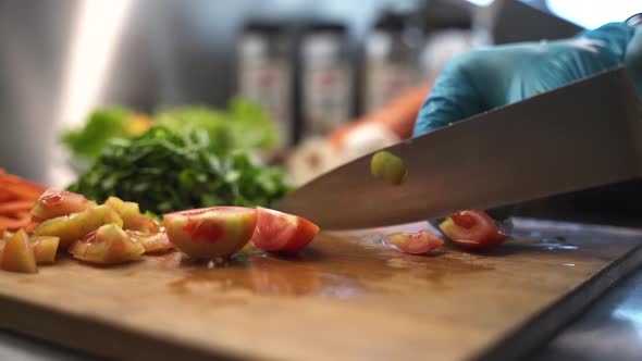 Chef slicing tomatoes on kitchen cutting board.