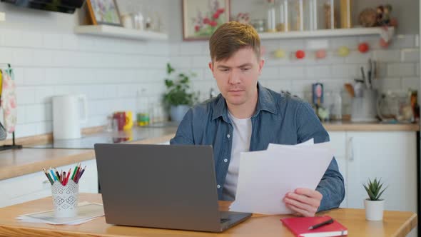 Young Man Reading Paper While using Laptop at home