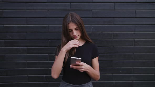 An Attractive Young Lady Wearing Glasses Using a Phone Against a Brick Wall Background. Close-up