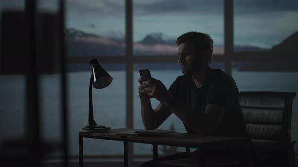 Silhouette of a Man Sitting at a Table Looking at a Mobile Phone Thinking and Analyzing the Stock