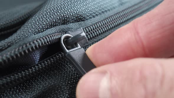 Fingers pull the zipper lock and close the green textile backpack