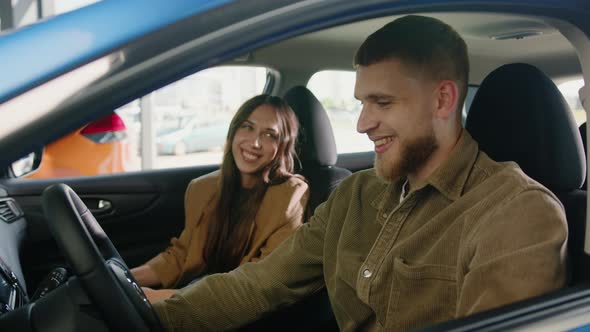 Happy Couple Looks at Each Other in a Good Mood Sitting in the Cabin a New Car