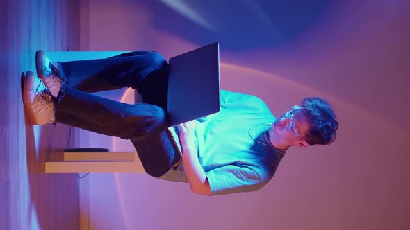 Lonely Stylish Man in Glasses Sits Working at a Laptop in Neon Lighting