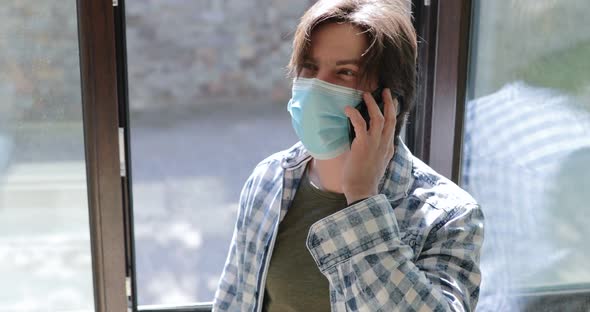 Man in Mask Breathes Fresh Air Near at Window and Speaking on Phone at Home