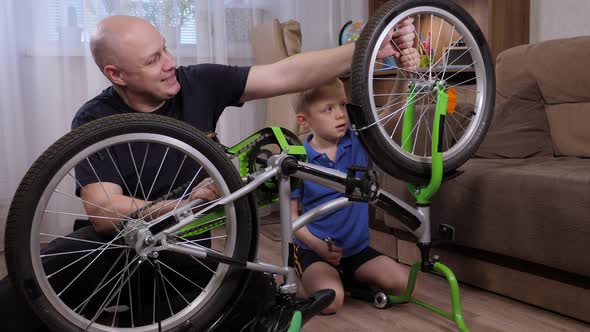 Portrait of a Young Father and His Son Repair a Broken Bicycle Together at Home