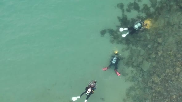 Arial view of three scuba divers underwater following each other using waterproof torches