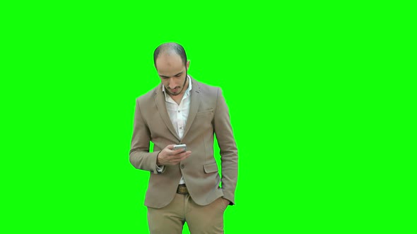 Business Man Walks in Texting on the Phone on a Green Screen, Chroma Key