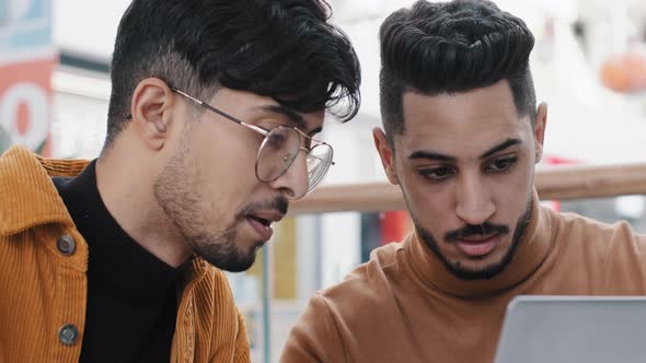 Two Young Arab Guys Friends Chatting Looking at Laptop Screen Making Order in Online Store Using New
