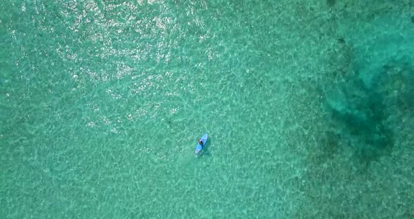 Aerial drone view of a man paddling an SUP stand-up paddleboard near a tropical island.