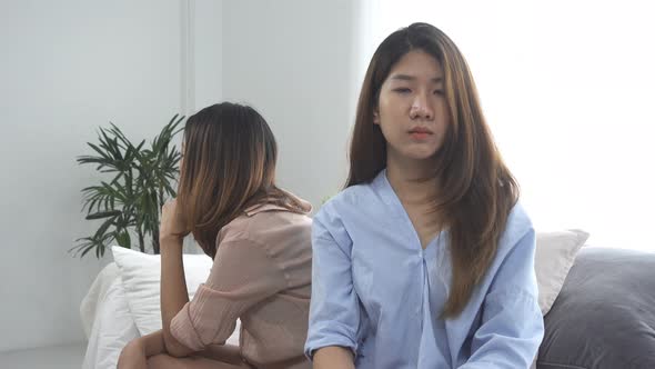 Asian lesbian lgbt couple sitting each side of sofa with moody emotion in living room.