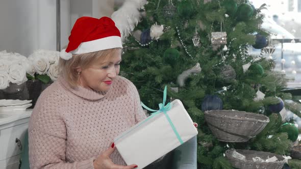 Happy Senior Woman in Santa Claus Hat Holding Christmas Present