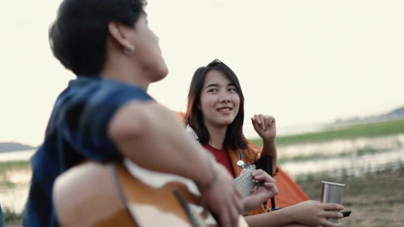 A happy young Asian couple camping playing the guitar and singing a song together.