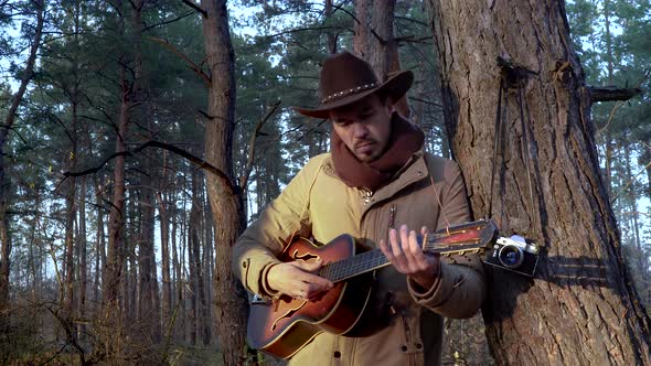 A Backpacker in a Hat with a Guitar in the Forest