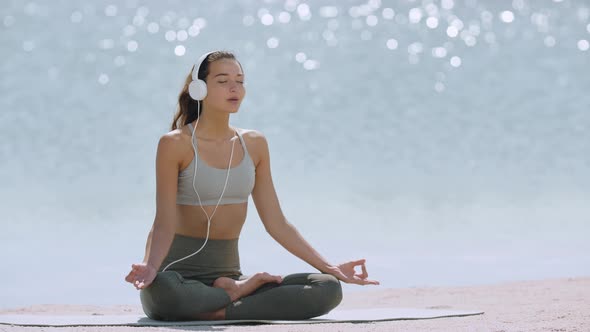 Woman in Yoga Meditation Pose with Headphones on the Beach