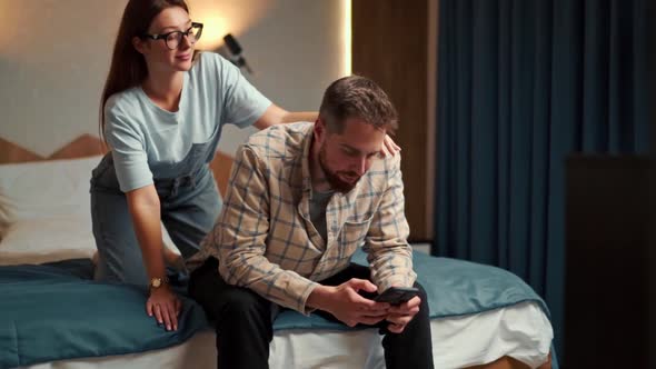 the guy works on the phone in the hotel room and the girl demands attention