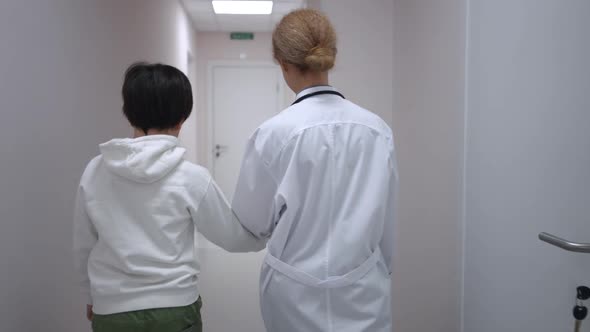 Positive Caucasian Pediatrician Talking to Patient Walking in Slow Motion to Office Along Hospital