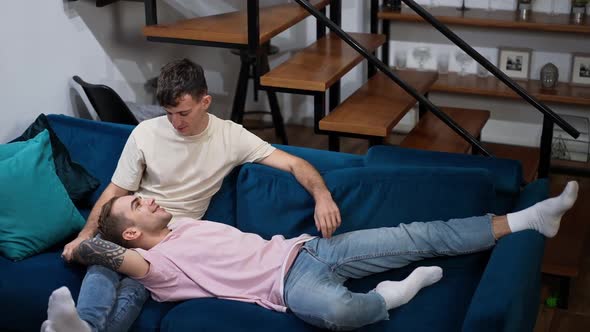 Relaxed Caucasian Gay Couple Lying on Soft Comfortable Couch in Living Room Talking