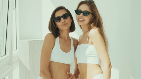 Portrait of two young beautiful smiling women in white lingerie posing at sunny summer day