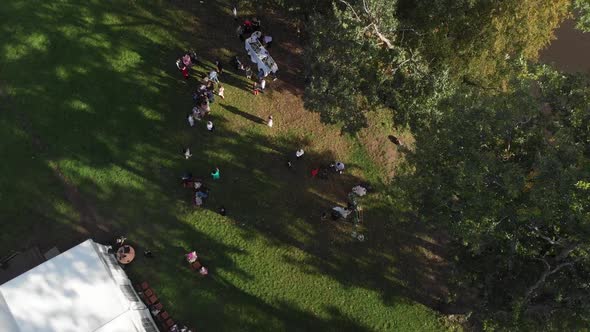 The Camera Flies High Above the Resting People on the Lawn on the River Bank