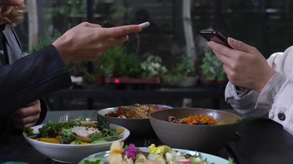 Two Pair of Hands Taking Pictures of Healthy Vegan Meals Served on Black Wooden Table