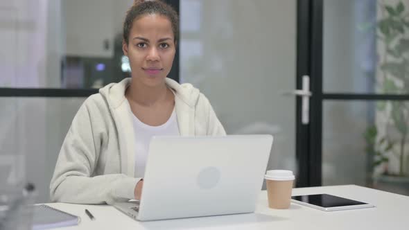 African Woman Looking at Camera While Using Laptop in Office