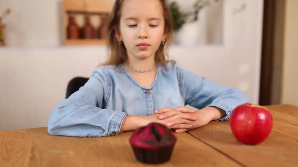 Little girl choosing fresh red apple against sweet cake