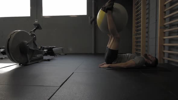 Young athletic man doing lower abs with a Pilates ball at the gym