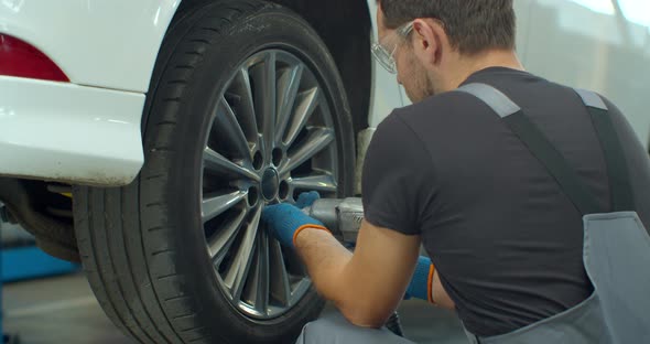 Mechanic Is Unscrewing Lug Nuts with a Pneumatic Impact Wrench. Specialists Removes the Wheel in