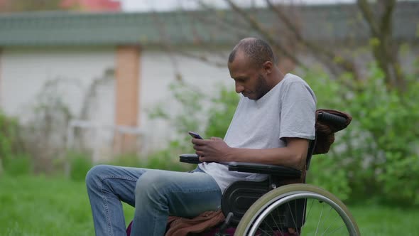 Medium Shot Side View of Paralyzed African American Man in Wheelchair Surfing Social Media on