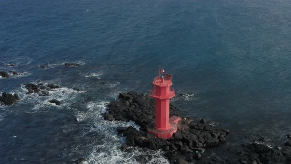 Drone view. The scenery is vast with sea, waves hitting rocks, and a lighthouse