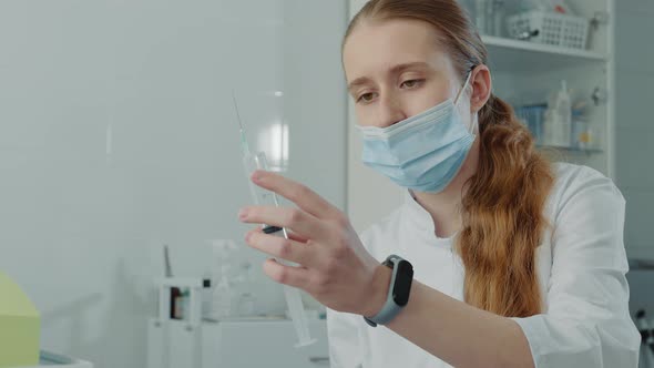 Young Nurse Trainee Holding a Large Syringe with Medicine and Examining a Syringe