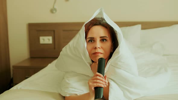 Young Woman Wrapped in Blanket Lying on Bed and Watching Tv