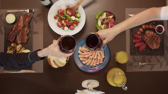 Couple of Glasses of Wine Clink Against the Background of a Table with Food