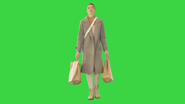 Young Woman in Grey Coat Walks with Paper Bags on a Green Screen Chroma Key